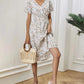 A woman models the Talore white V-neck midi dress featuring a ditsy floral print, short flutter sleeves, and a cinched waist, accessorized with a straw bag and white sandals. This lifestyle shot showcases the dress's flowy silhouette in a natural setting.