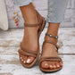 Women's tan vegan leather strappy flat sandals with delicate straps and an antique gold buckle, worn with blue jeans and a turquoise beaded anklet.