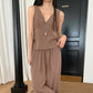 A woman models a muted taupe sleeveless V-neck crepe set featuring a gathered bust top and flowy wide-leg drawstring trousers, styled with a long necklace.