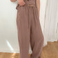 Muted taupe two-piece resort set featuring a sleeveless V-neck top with gathered bust and flowy wide-leg trousers on a female model in a studio setting.