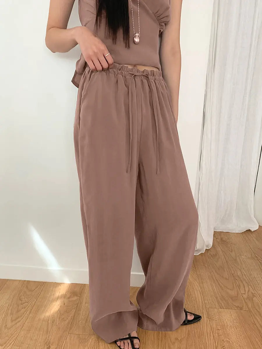 Muted taupe two-piece resort set featuring a sleeveless V-neck top with gathered bust and flowy wide-leg trousers on a female model in a studio setting.