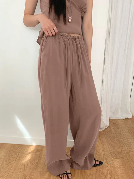 Muted taupe two-piece resort set featuring a sleeveless V-neck top with gathered bust and flowy wide-leg trousers on a female model in a studio setting.