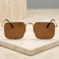 Front three-quarter view of Tavren vintage square sunglasses with gilded gold metal frames and mocha brown tinted lenses, resting on a textured stone surface.