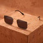 Elegant vintage square sunglasses with gilded gold metal frames and dark grey lenses, angled on a textured terracotta block.