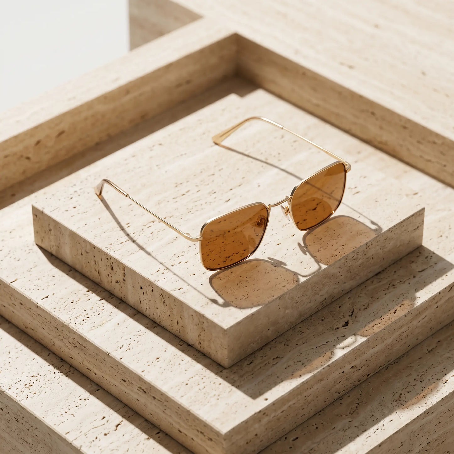 Tavren vintage chic square sunglasses with gilded gold ultra-thin metal frames and amber yellow lenses, artfully presented on a stepped travertine display.