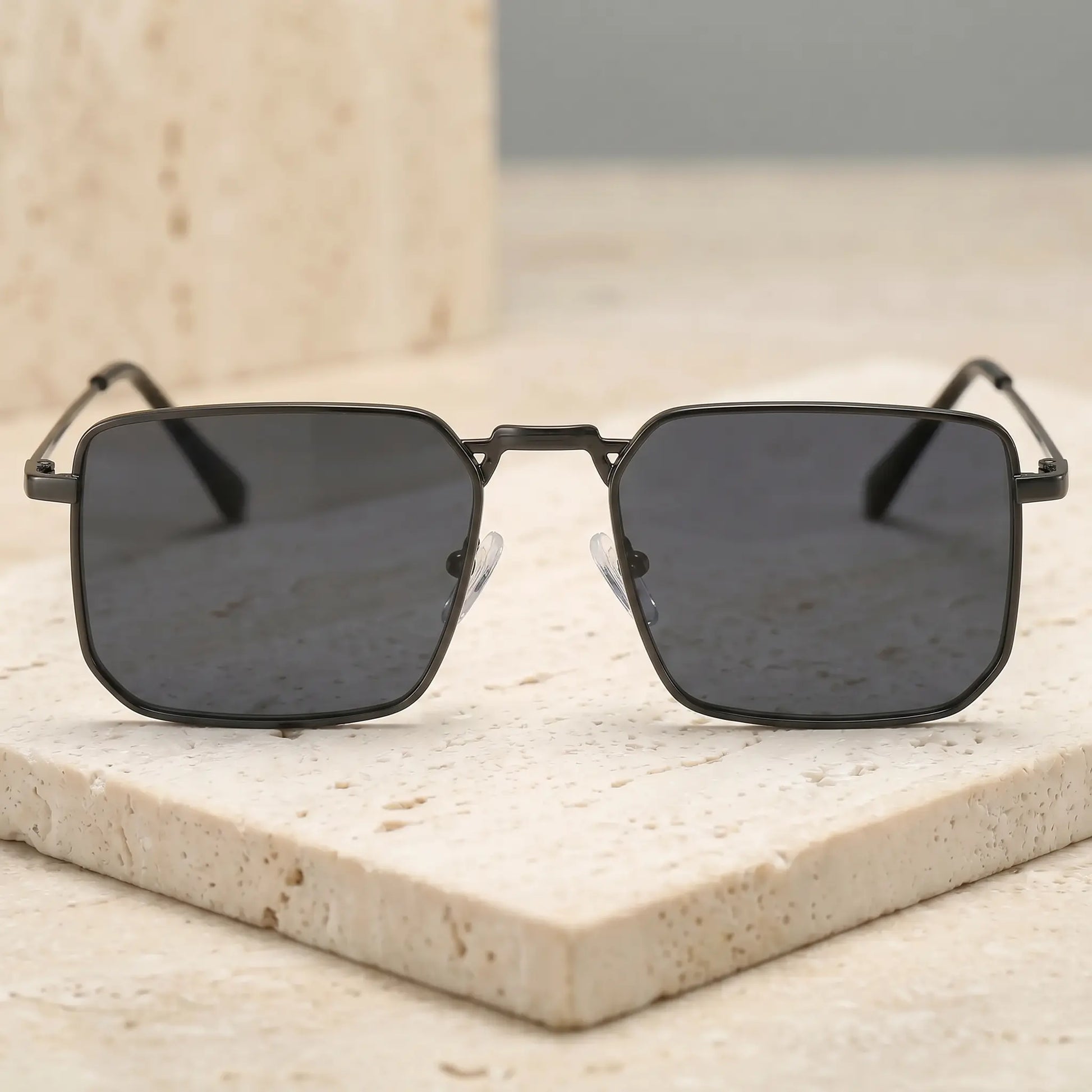 Tavren vintage square sunglasses with an onyx black metal frame and slate grey lenses, shown from a three-quarter angle on a textured surface.