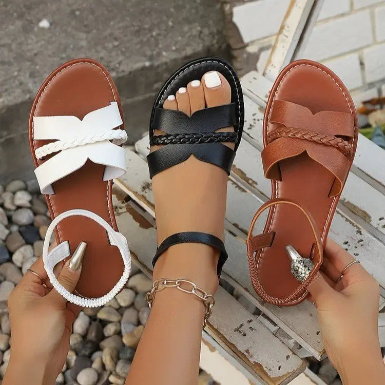 Three pairs of Tavri flat braided summer sandals in white, black, and brown, shown on feet with braided straps, ankle straps, and tan footbeds. Open-toe design with black rubber soles.
