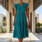 Elegant model wears a Teal Blue Torvun Ruffled Tiered Midi Dress. Features a V-neck, flutter cap sleeves, and a flowing three-tiered skirt, styled in a luxurious outdoor setting.