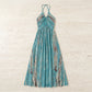 Teal tie-dye halter maxi dress, laid flat. Features a gathered neckline, flowing A-line silhouette, and vertical pattern of white ovals and brown dotted stripes.