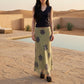 Female model in Thalwyn navy V-neck knit top and sage green abstract mesh maxi skirt, showcasing the flowing silhouette and unique patterns in a warm desert resort setting.