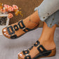 Black Torquin platform slide sandals with a textured interlocking strap design and gold-tone hardware, shown on a woman's foot with an ankle bracelet and denim jeans.