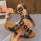 Black platform slide sandals with interlocking textured faux leather straps and gold-tone hardware, shown from a three-quarter angle on a foot with manicured nails.