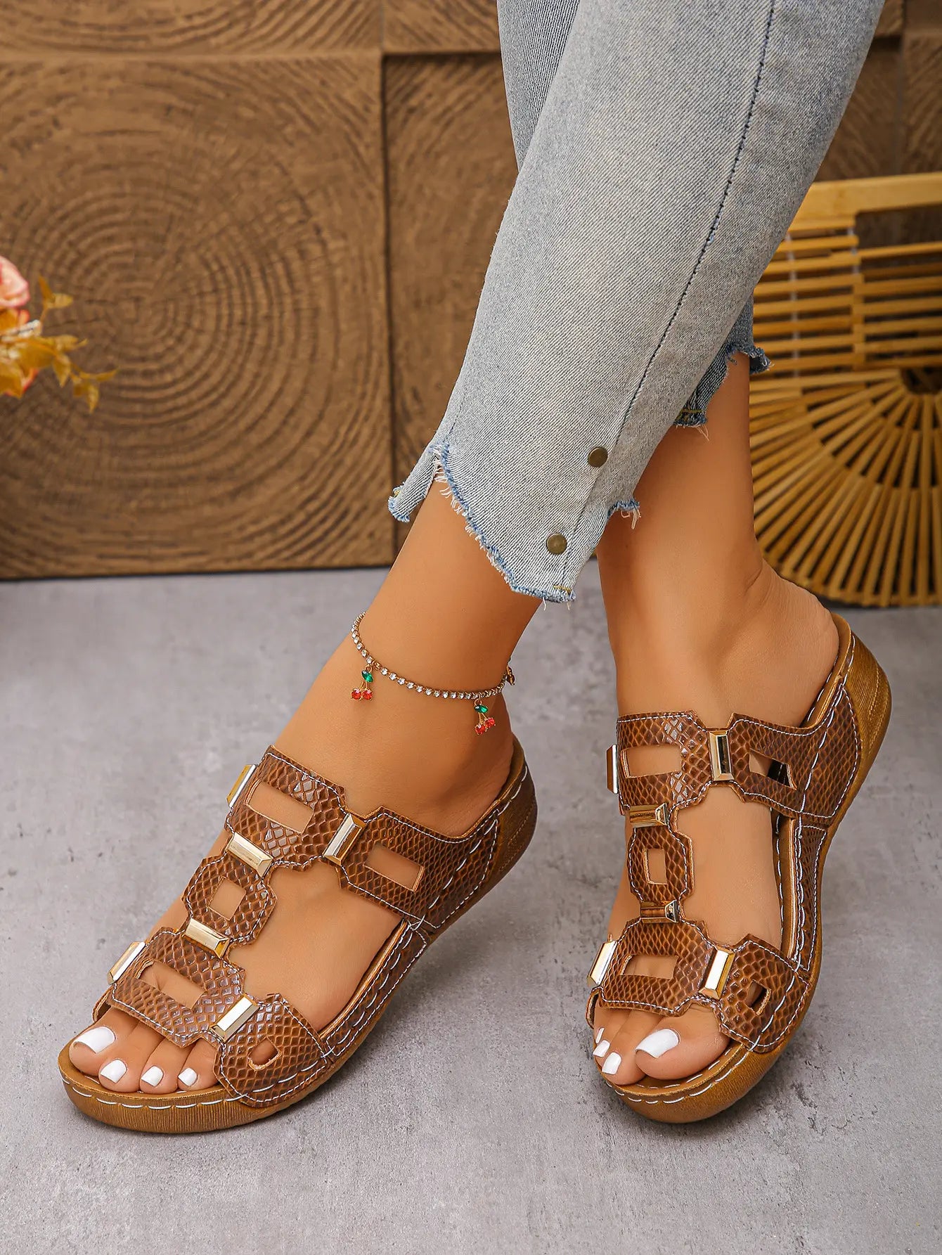 Women's brown slide platform sandals featuring interlocking textured straps with gold-tone hardware, detailed white contrast stitching, and a contoured footbed, worn by a model with cropped jeans.