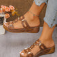 Brown textured synthetic leather platform slide sandals with interlocking straps and gold-tone hardware are worn by a model with ripped jeans, styled with flowers.