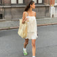 Woman wearing a white cotton camisole and shorts set, walking outdoors with a tote bag and drink, styled casually with sneakers. The camisole features spaghetti straps and a relaxed fit. A perfect representation of bohemian summer comfort.