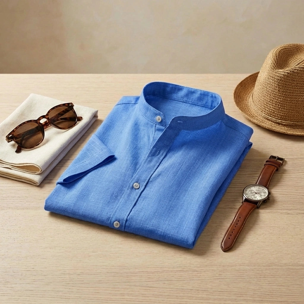 Vandore Imperial Blue mandarin collar shirt in linen-weave texture, styled with a straw hat, watch, and sunglasses on a wooden table.