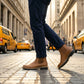 Vantor Classic Chelsea Boots in burnished tan microfiber leather walking on a cobblestone street with yellow taxis in the background.