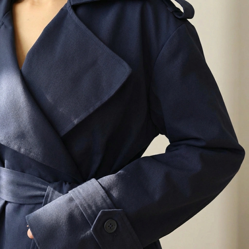 Varelle structured short trench coat in navy blue — close-up detail showing the oversized architectural lapel, button-tab cuff, and belted waist texture.