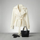 Varelle structured belted short trench coat in cream cotton blend — front view showing oversized lapels and cinched waist, styled with black handbag and gloves.