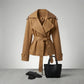 Varelle structured short trench coat in camel cotton blend — front view showing wide lapels and belt, styled with black handbag and gloves.