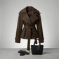 Varelle structured short trench coat in dark brown cotton blend featuring a belted waist and oversized lapels, styled with a black tote bag and gloves.