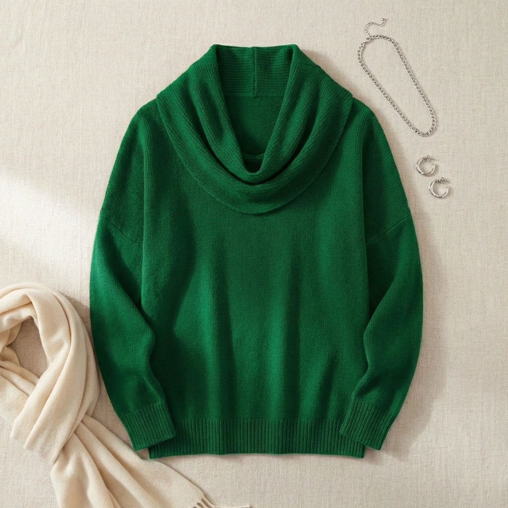 Vellura soft cowl neck knit sweater in emerald green, flat lay view showing the draped neckline and ribbed cuffs styled with silver accessories.