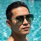 VELORA retro aviator sunglasses in emerald green fade worn by a man in a pool, showing water droplets on the gradient lenses.