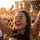 Woman wearing VELORA oversized aviator sunglasses with amber gradient lenses and glitter makeup at a sunny music festival.