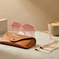 VELORA oversized aviator sunglasses in Rose Quartz pink with gold double-bridge frames and gradient lenses, resting on a branded leather case.
