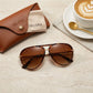 VELORA oversized aviator sunglasses in vintage tortoise shell, flat lay view with branded leather case and cleaning cloth on stone surface.