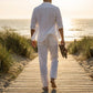 Ventoso men's linen trousers in white, back view showing rear patch pockets and relaxed straight-leg fit walking on a beach boardwalk.