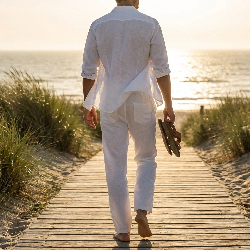 Ventoso men's linen trousers in white, back view showing rear patch pockets and relaxed straight-leg fit walking on a beach boardwalk.