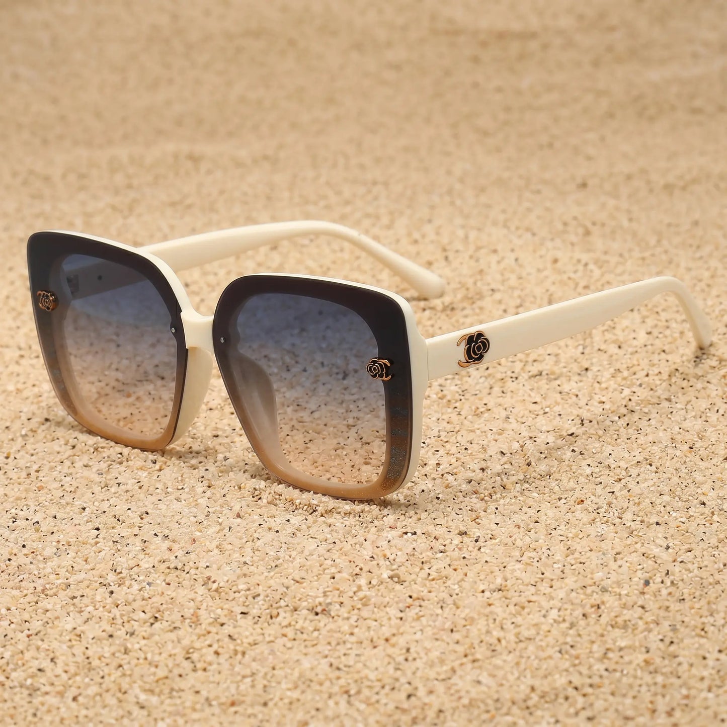 Vesryn oversized square sunglasses with off-white temples, amber gradient front frame featuring subtle stripes, and gradient grey lenses. Gold floral metal accent on temples.