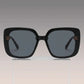 Vesryn oversized square sunglasses with thick black acetate frames and dark gradient grey lenses, featuring gold floral-inspired metal logo accents on the temples.