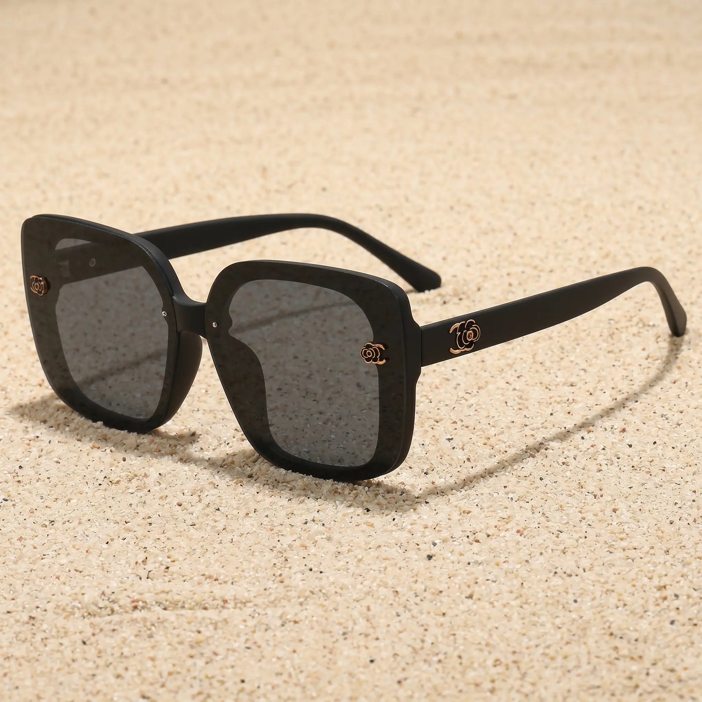Oversized square black sunglasses with gradient grey lenses and gold floral accents on the temples. Presented on a clean white background.