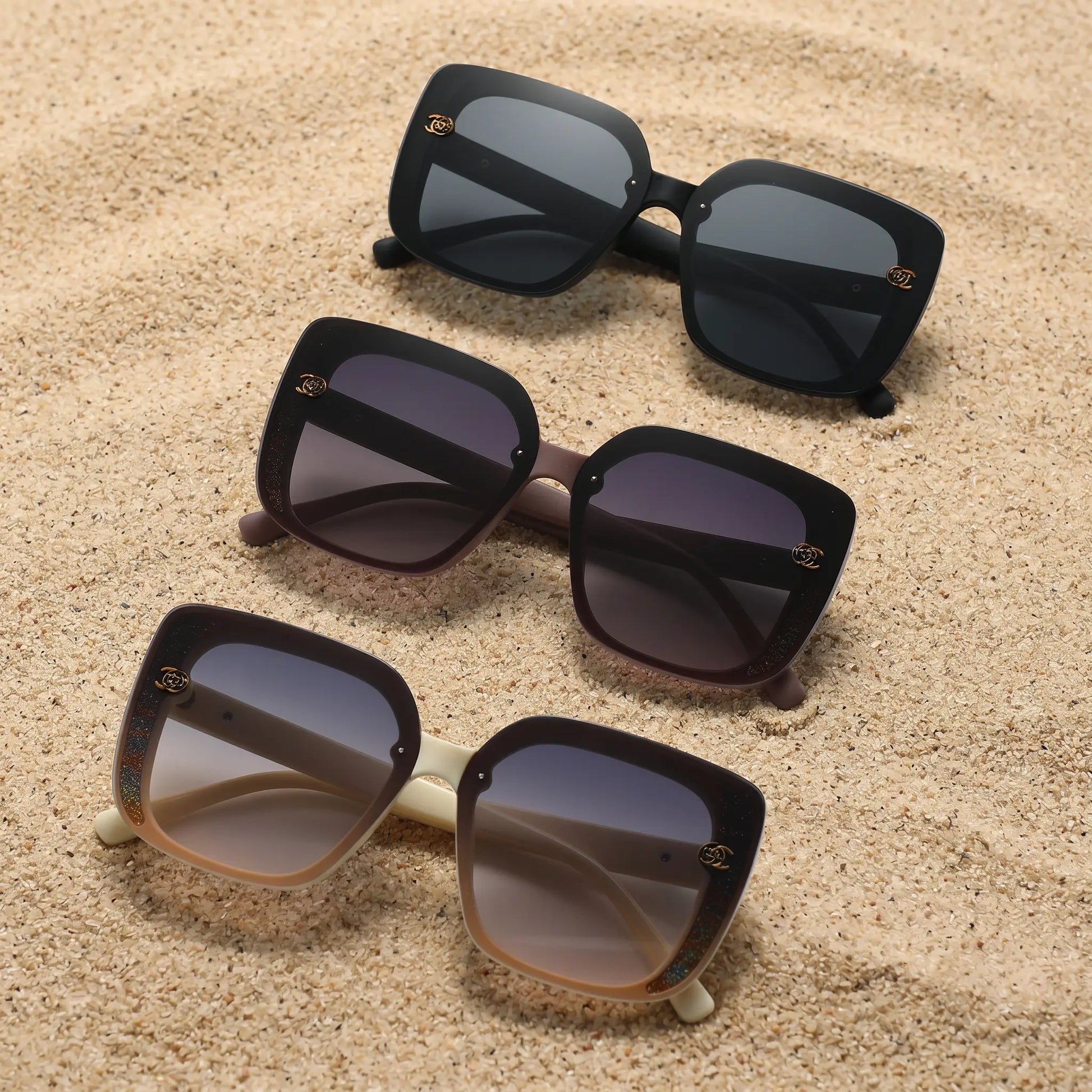 Vesryn oversized square sunglasses collection showcasing three pairs in black, brown, and cream with gradient lenses and floral-inspired gold accent details.