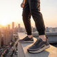 Vexor men's shock absorbing sneakers in black microfiber leather worn on a city rooftop, side view showing the thick beige EVA sole.