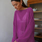 Female model wearing a vibrant rose sheer bell sleeve knit sweater with a boat neck, styled over a white bralette, in an indoor setting.