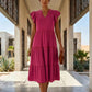 Female model walks forward, wearing a Vibrant Rose Torvun Ruffled Tiered Midi Dress with V-neck and flutter cap sleeves. The dress features a three-tiered skirt, styled in an elegant outdoor architectural setting.