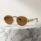 Gold-toned vintage oval metal frame sunglasses with brown tinted lenses and tortoiseshell temple tips, presented on a marble pedestal.