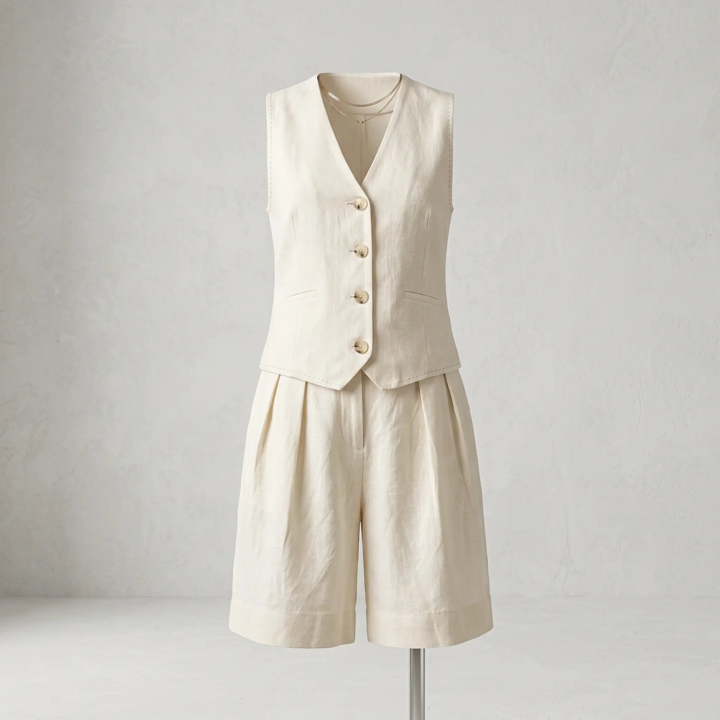 Creamy ecru linen-blend tailored vest and wide-leg pleated shorts set, front view on mannequin with mother-of-pearl buttons and cuffed hem.