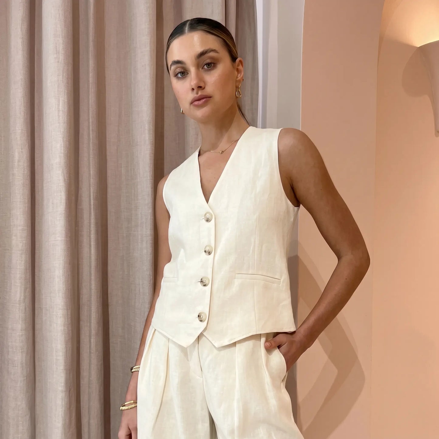 Vorien women's chic linen blend set in creamy ecru, featuring a sleeveless V-neck vest with mother-of-pearl buttons and high-waisted, wide-leg pleated shorts with cuffed hems, shown on a model.