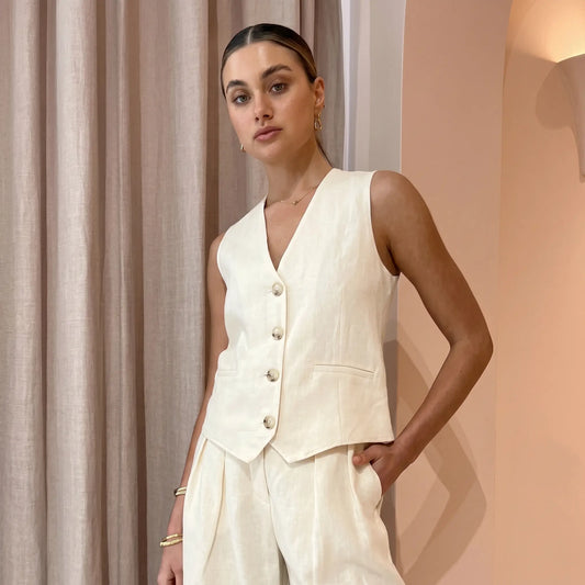 Vorien women's chic linen blend set in creamy ecru, featuring a sleeveless V-neck vest with mother-of-pearl buttons and high-waisted, wide-leg pleated shorts with cuffed hems, shown on a model.