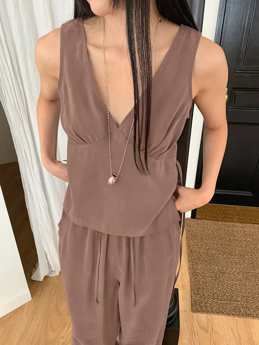 A woman models a muted taupe sleeveless V-neck flowy resort set featuring a gathered bust top and wide-leg elastic drawstring trousers.
