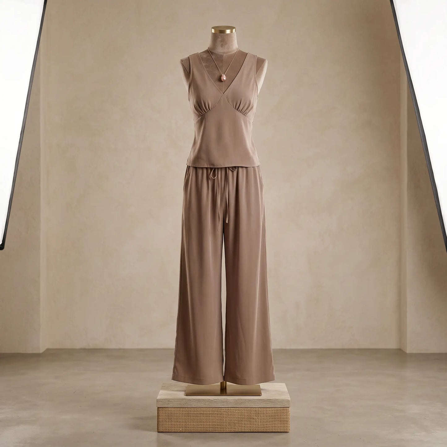 Vorlag taupe V-neck sleeveless flowy resort set with wide-leg trousers on a mannequin, showcasing its fluid drape and relaxed silhouette. This elegant two-piece is styled with a delicate necklace.