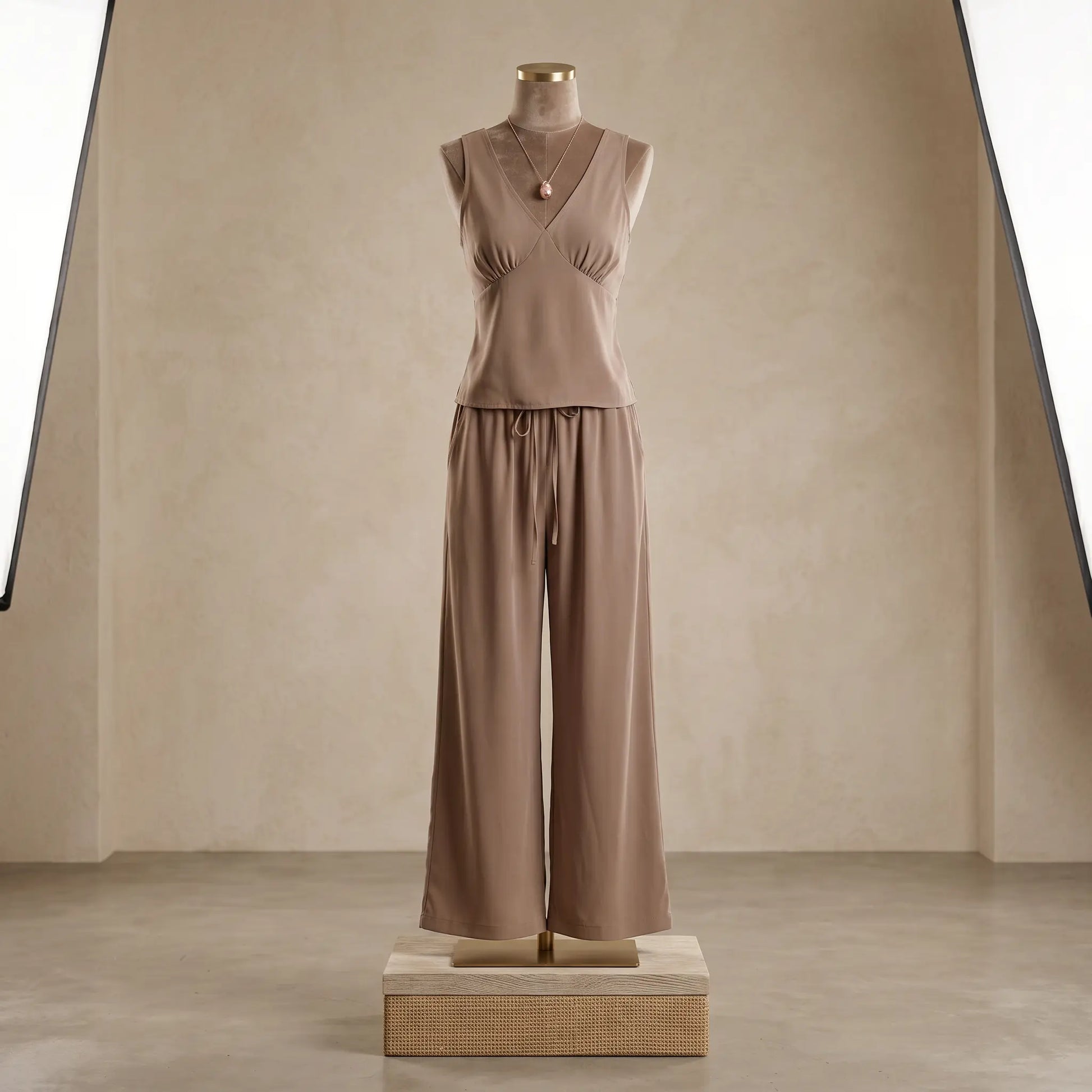 Vorlag taupe V-neck sleeveless flowy resort set with wide-leg trousers on a mannequin, showcasing its fluid drape and relaxed silhouette. This elegant two-piece is styled with a delicate necklace.