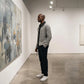 Vornex hybrid denim knit cardigan in gray worn by a man in an art gallery — side profile showing the heavy ribbed texture and structured fit.