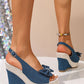 Vykos dark denim-like wedge espadrille sandals with a crystal bow embellishment and adjustable slingback strap, shown from a three-quarter view on a foot.