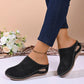 Black perforated wedge mules worn by a model, showcasing the comfortable slip-on design with a rounded toe and medium wedge heel, styled with denim jeans.