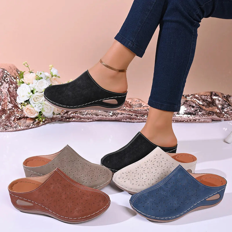 Vylos comfortable wedge mules with perforated floral uppers in black, cream, brown, khaki, and blue, shown on a model's foot with multiple colors displayed.